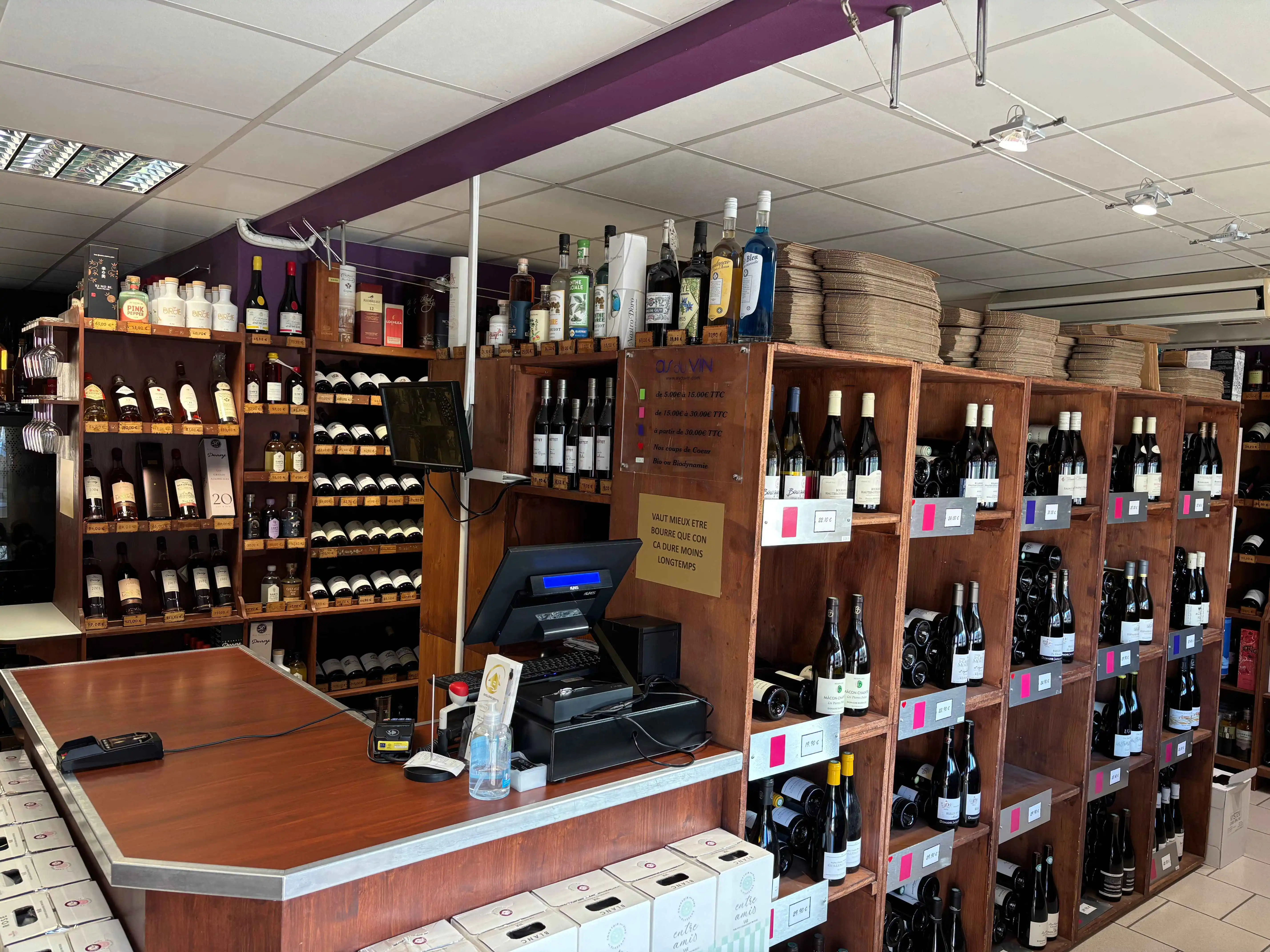 Intérieur de la cave à vins As du Vin à Dijon, présentant une large sélection de crus de Bourgogne et spiritueux sur des étagères en bois.